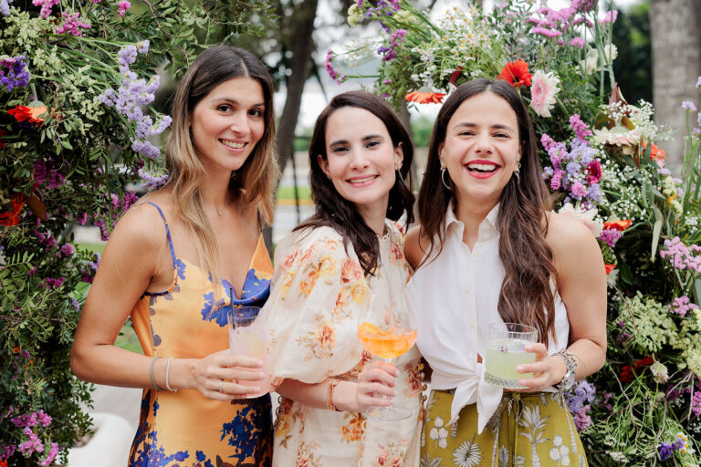 Τρεις φίλες μοιράζονται μια αυθεντική στιγμή χαράς με κοκτέιλ μπροστά από μια εντυπωσιακή floral εγκατάσταση σε μια καλαίσθητη δεξίωση βάπτισης, από τον Ignatios Kourouvasilis. Βάπτιση Άγιος Γεώργιος Καβούρι | Ignatios Kourouvasilis